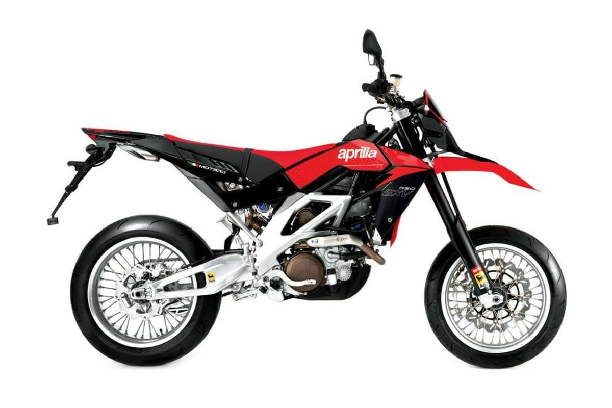 2010 Aprilia SXV 550 supermoto in red and black, right-side studio profile showing spoked wheels, inverted forks and twin underslung exhaust