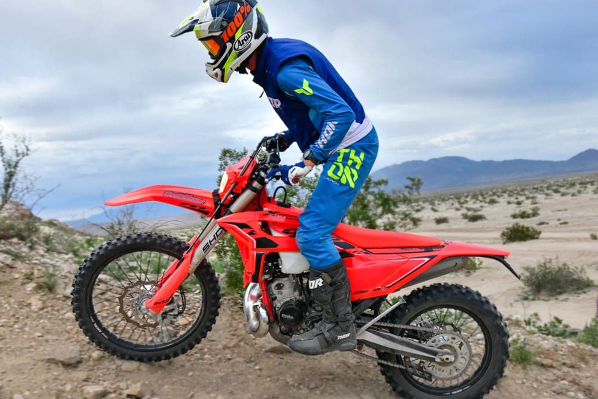 Rider in blue Thor gear powering the red Beta 200 RR X-Pro up a rocky desert trail, front wheel lofted over loose rock