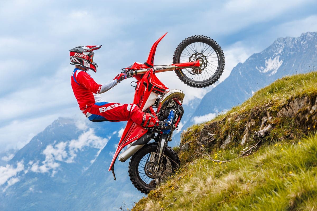 Beta 250 RR X-Pro rider leaning back into a steep mountainside wheelie, front tire lifted high with snow-capped peaks in the distance