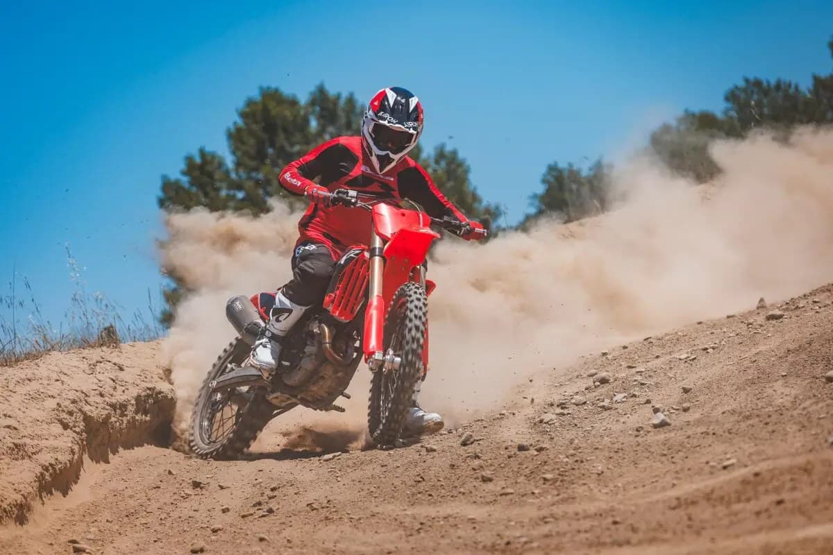 Rider in red Beta gear leaning into a berm on the 250 RXF, front wheel kicking up a wall of dust against a blue sky