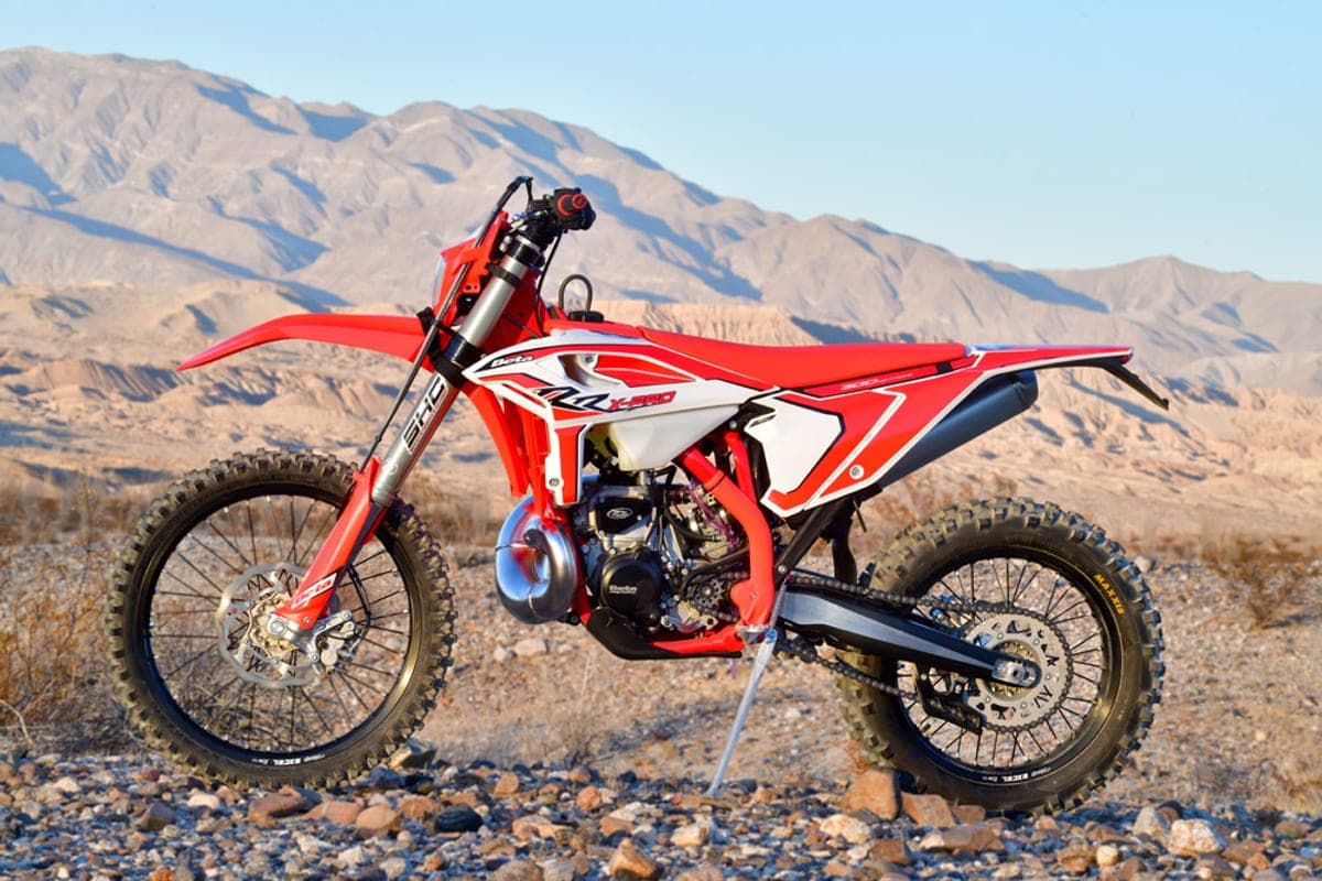 Beta 300 RR X-Pro parked on a rocky desert trail with mountains behind it, red and white bodywork and kickstand deployed on gravel