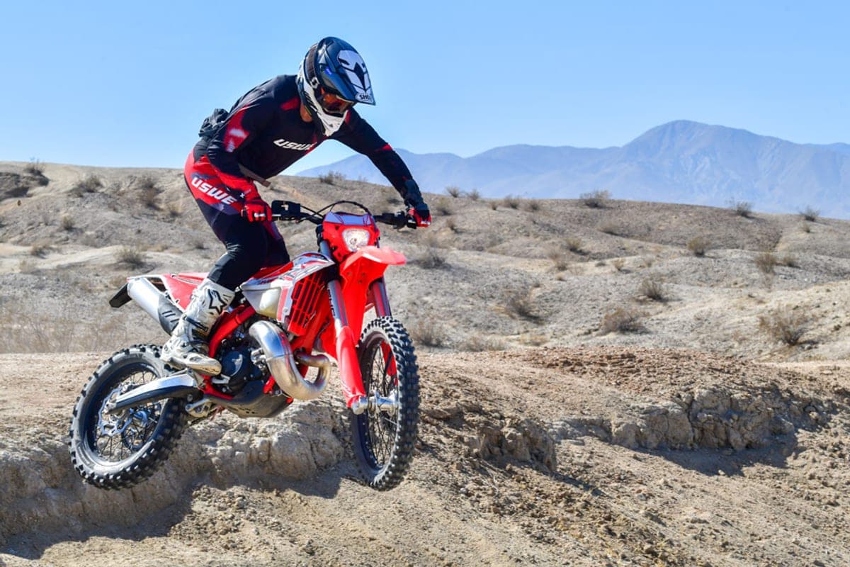 Rider in black and red USWE gear leaning into a berm on a Beta 300 RR X-Pro, dust kicking up from the rear knobby tire on a sandy hillside