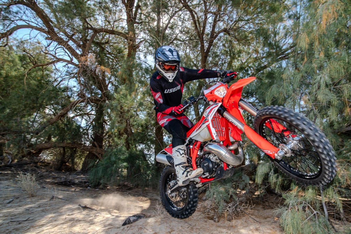 Beta 300 RR X-Pro getting air off a jump in a wooded desert wash, rider in full gear with front wheel lifted and trees framing the shot