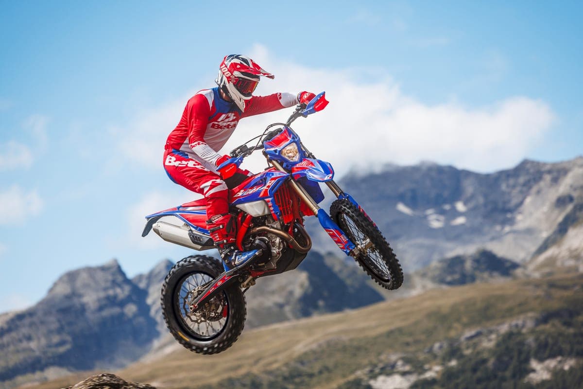 Rider in red and white Beta gear launching the 350 RR Race off a jump with mountains in the background, front wheel tucked mid-air