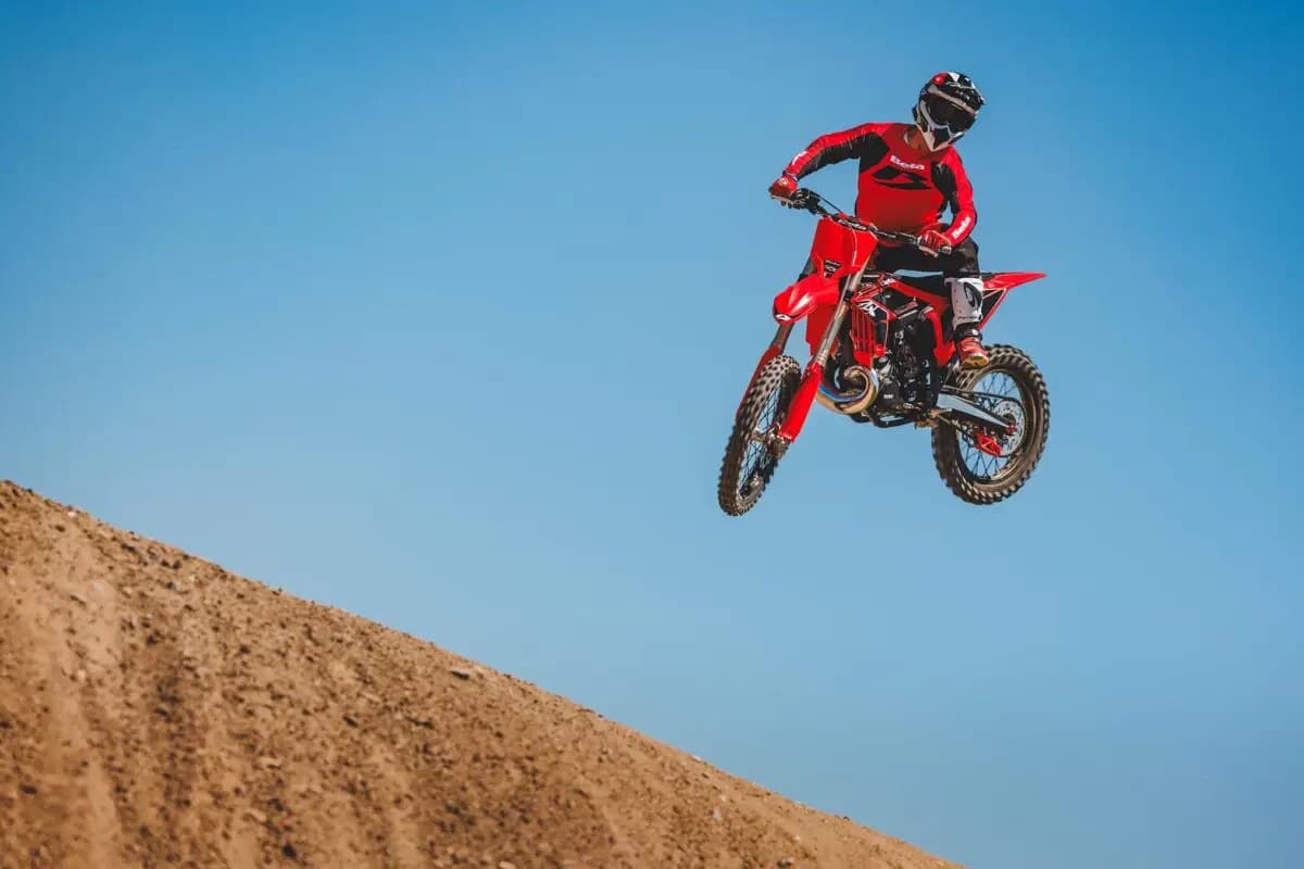 Rider in matching red Beta gear launching a 350 RX high off a dirt jump against a clear blue sky at a motocross track