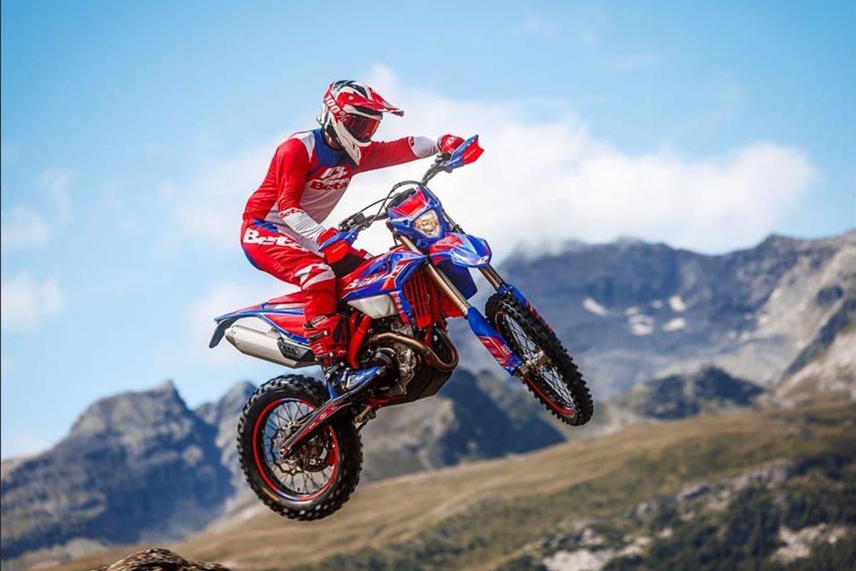 Rider in red and white Beta gear launching the blue and red 390 RR Race off a jump against a mountain backdrop