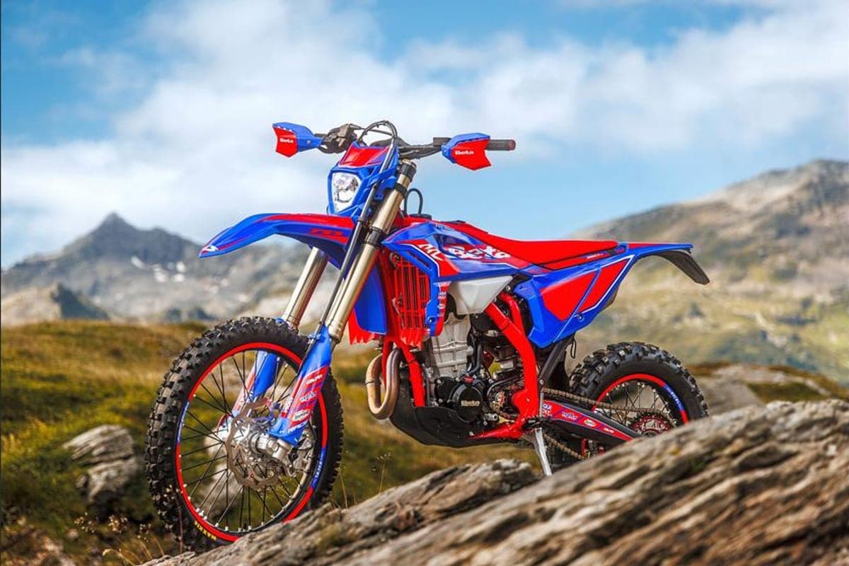 Beta 390 RR Race parked on a boulder with blue bodywork, red-rimmed wheels and headlight visible against alpine peaks