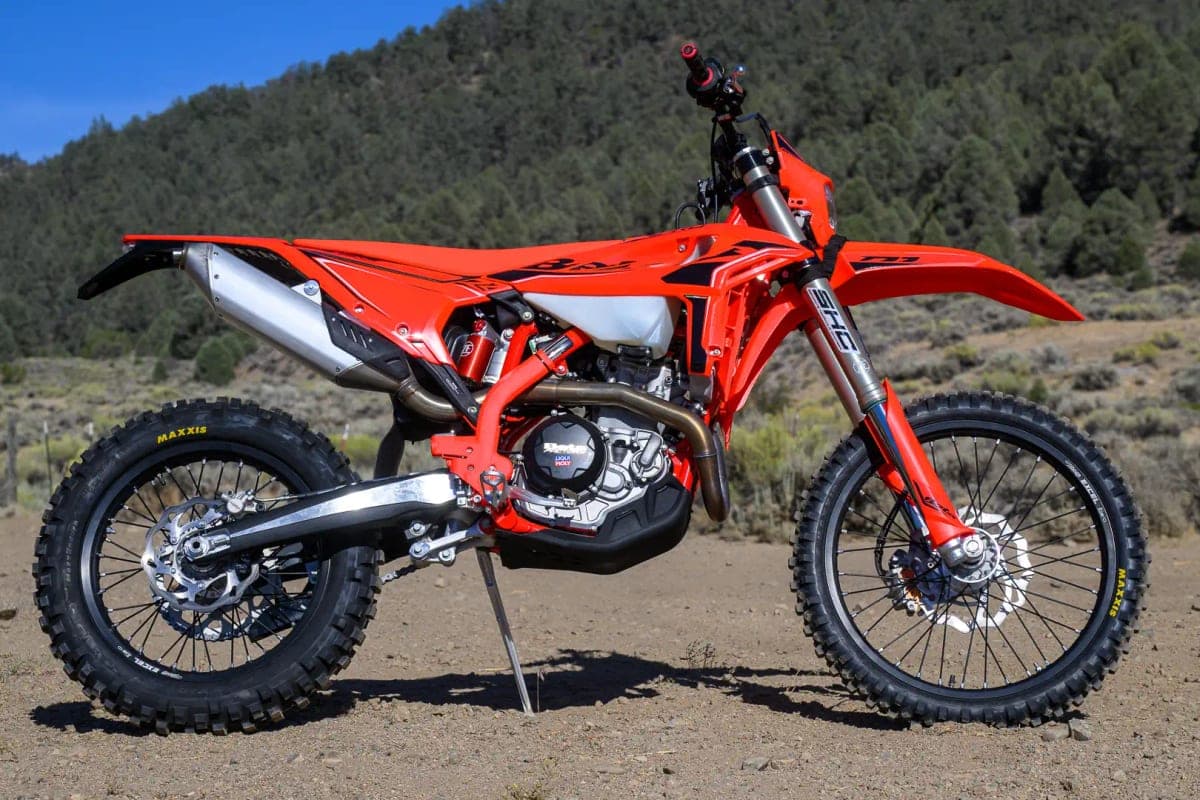 Beta 390 RR X-Pro in red with black graphics, right-side outdoor profile against a pine-covered hillside, highlighting the tucked exhaust and red trellis frame