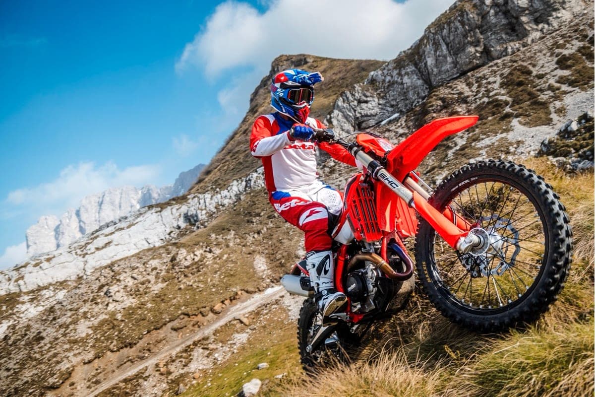 Rider in red, white and blue Beta gear climbing a rocky mountain trail on a red 430 RR X-Pro, front wheel lifted over loose scree