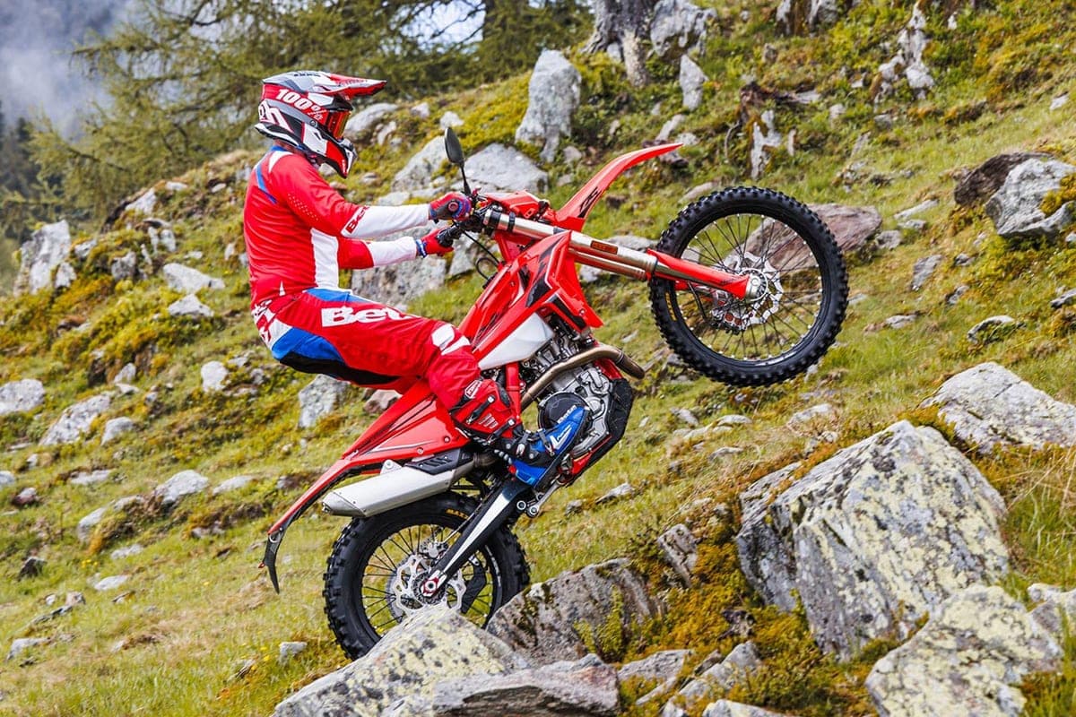 Rider in red and white Beta gear lofting the front wheel of a 430 RS up a rocky, moss-covered mountain trail