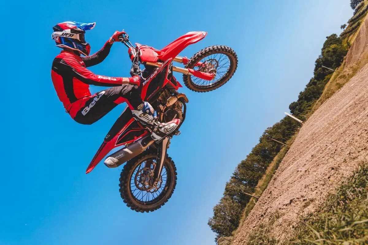 Rider in red and black Beta gear whipping a 450 RXF sideways mid-air against a clear blue sky above a dirt track berm