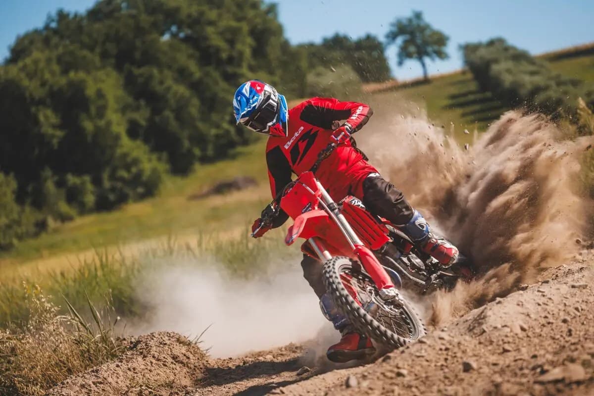 Beta 450 RXF rider in red gear leaning into a dirt corner, rear wheel kicking up a heavy roost of sand and dust