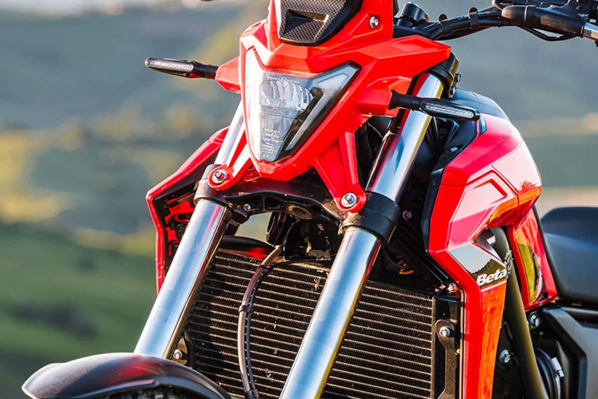 Close-up of the Beta Alp 4.0 front end at golden hour, showing the square LED headlight, oil cooler and 43mm fork legs