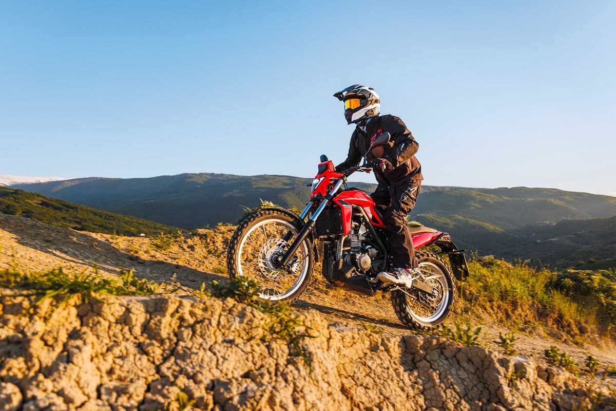 Rider in black gear climbing a rocky ridge on a red Beta Alp 4.0 at sunset, green hills behind