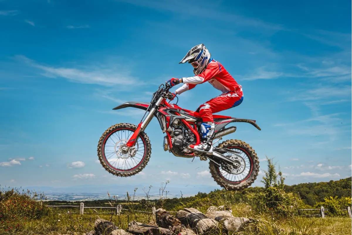 Rider in red and white gear launching a Beta Xtrainer 300 off a rocky trail feature, front wheel high in the air against a blue sky