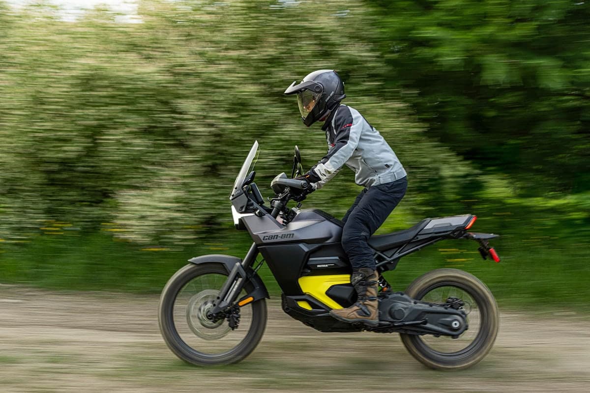 Can-Am Origin being ridden along a dirt trail past blurred green foliage