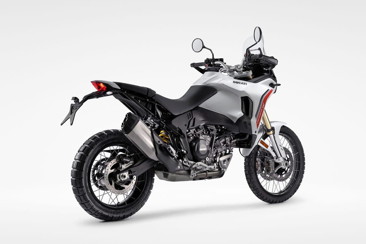 Ducati DesertX V2 in white and red, rear three-quarter studio view highlighting the twin-exit exhaust, gold shock and knobby off-road tires