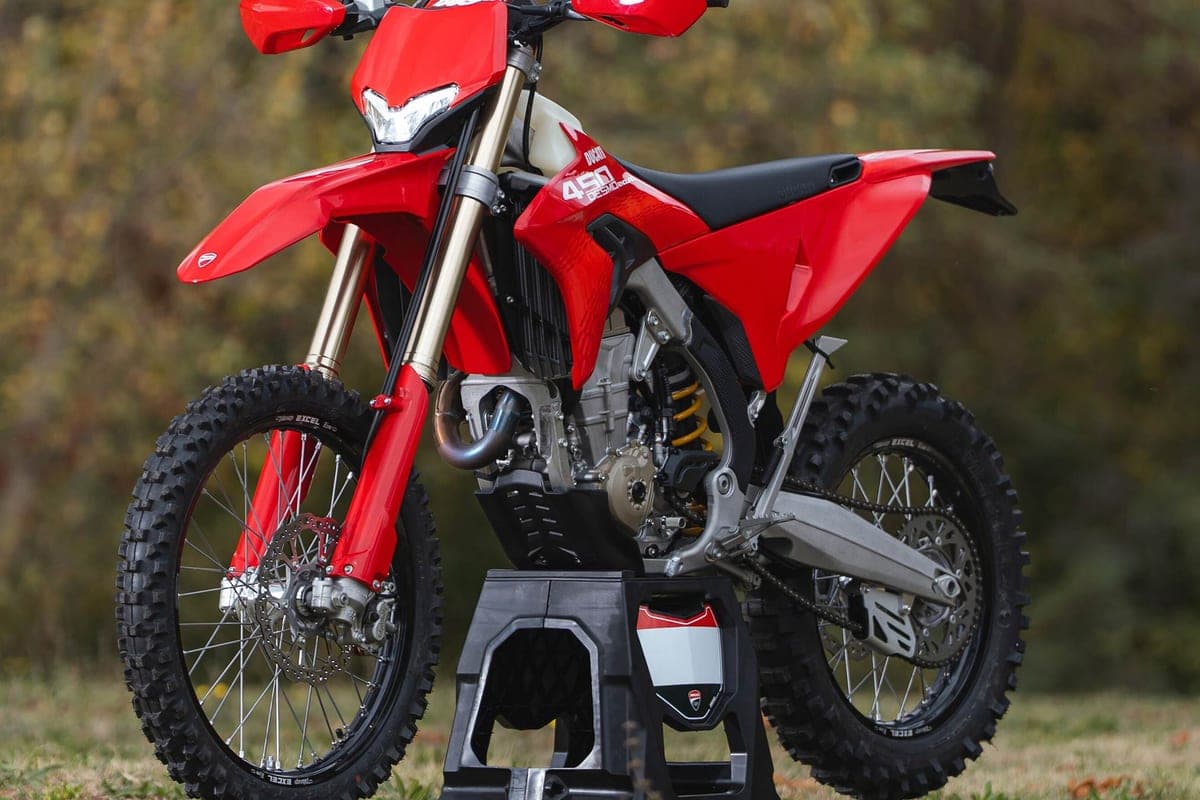 Ducati Desmo450 EDS front three-quarter shot on a stand outdoors, red bodywork with white tank panel, gold fork tubes and spoked wheels visible