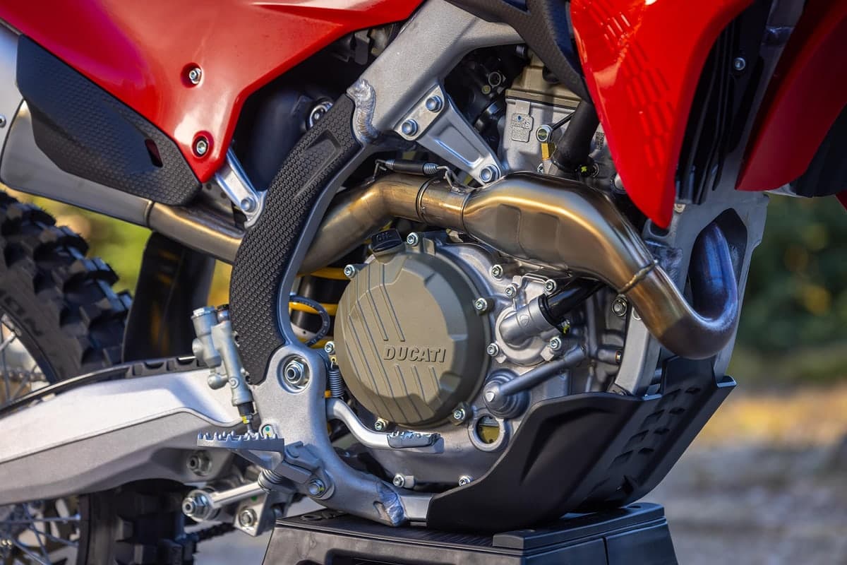 Detail shot of the Desmo450 EDX engine cradle showing the Ducati-marked crankcase cover, exhaust header pipe and aluminum frame spars