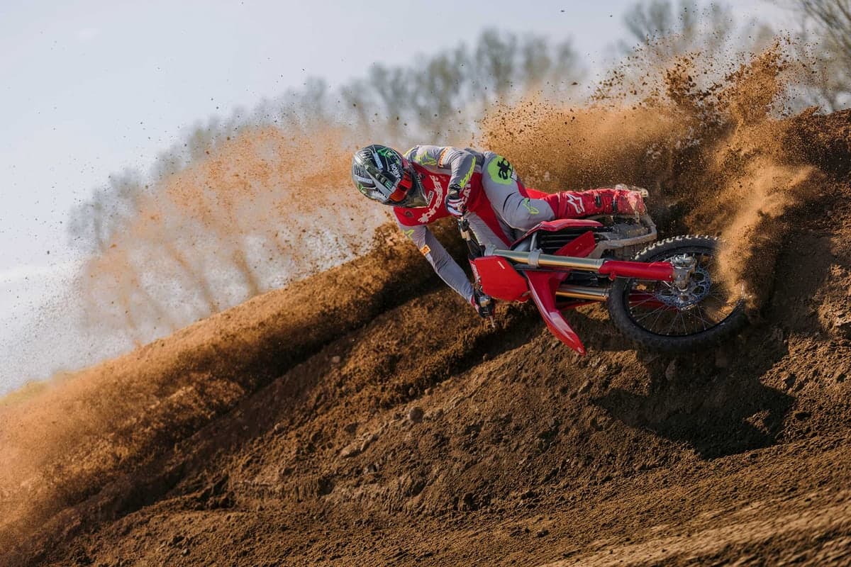 Rider in red and grey Alpinestars gear leaning the red Ducati Desmo450 MX through a hard dirt berm, kicking up a wall of roost