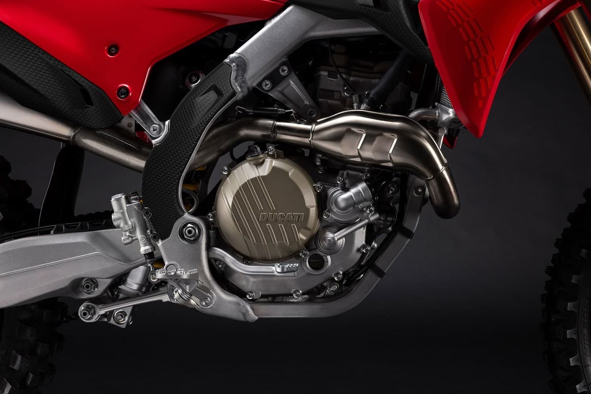 Close-up of the Ducati Desmo450 MX engine bay showing the titanium exhaust header, gold clutch cover and Ducati-branded crankcase