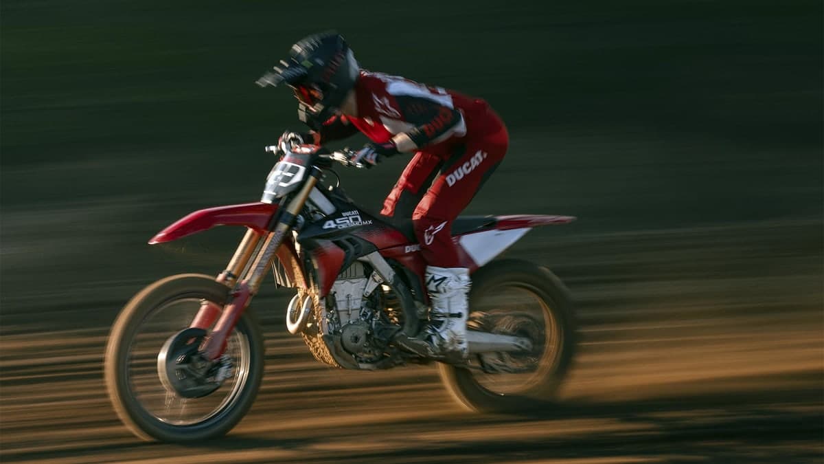 Ducati Desmo450 MX Factory catching air on a motocross track, rider in red and white Ducati Corse gear tucked low over the bars