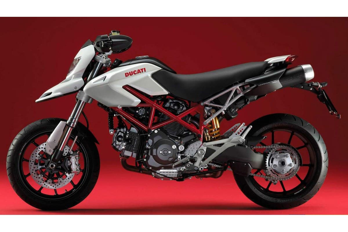 Ducati Hypermotard 1100 in white with red trellis frame, left-side studio profile on a red background showing gold forks and single-sided swingarm