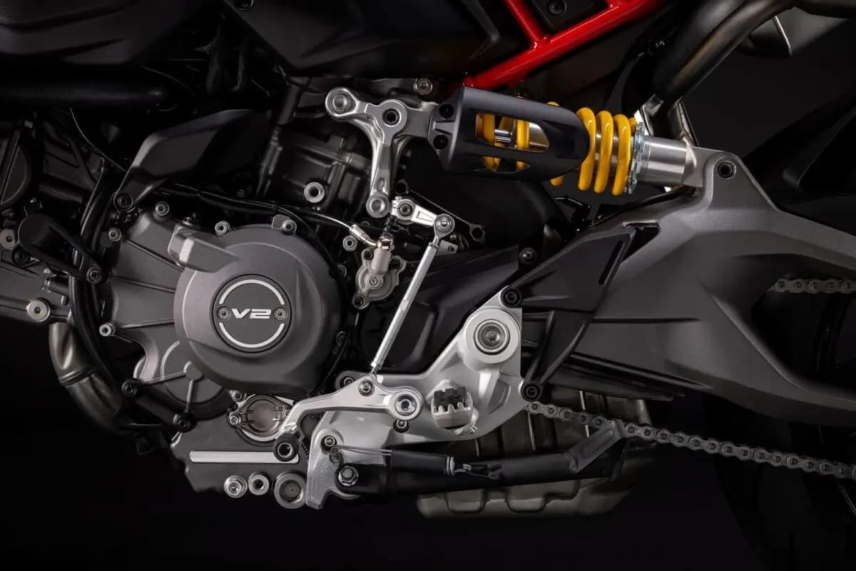 Ducati Hypermotard V2 close-up of the rear shock and swingarm, showing the yellow-spring monoshock, V2 engine cover badge and drive chain