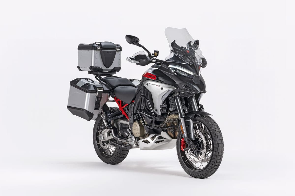 Ducati Multistrada V4 Rally front three-quarter view fitted with silver aluminum panniers and top case, tall clear windscreen and knobby dual-sport tires