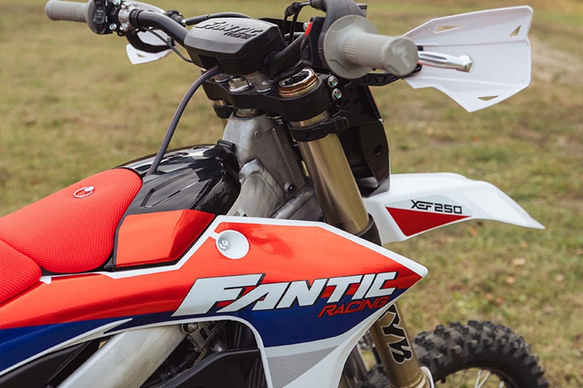 Fantic XEF 250 TL cockpit close-up with white handguards, black bark busters and red Fantic Racing tank graphics on grass