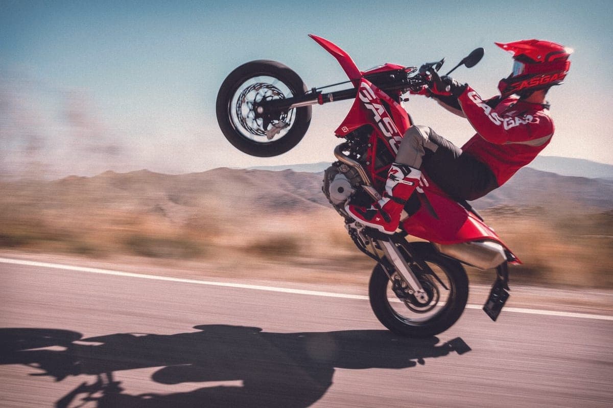 Rider in red GasGas gear wheelieing the ES 700 down a paved desert road, front wheel raised and motion-blurred scenery behind