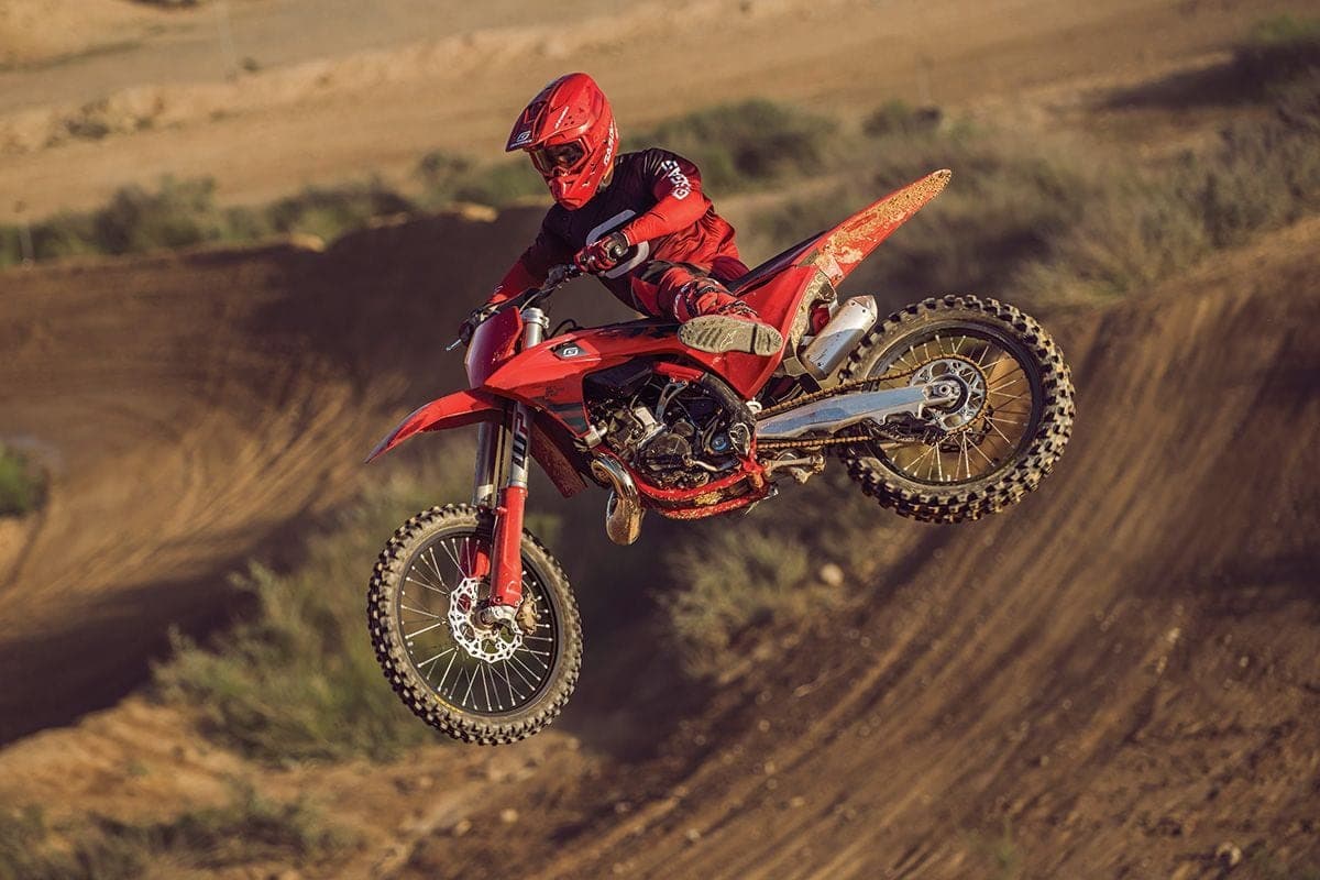 Rider in matching red gear launching a red GasGas MC 125 off a motocross jump, kicking up trailing dirt