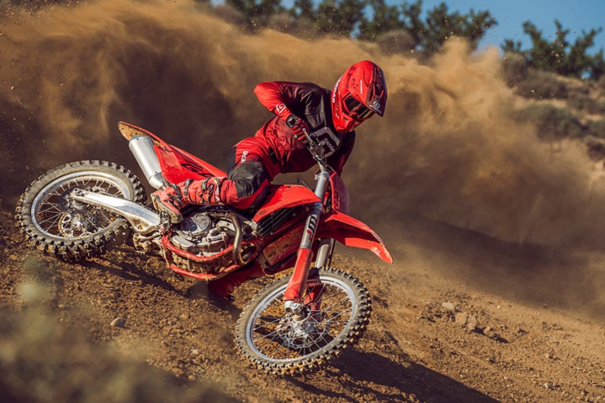 Rider in red and black gear leaning into a berm on a red GasGas MC 250F, kicking up a huge cloud of dust and dirt