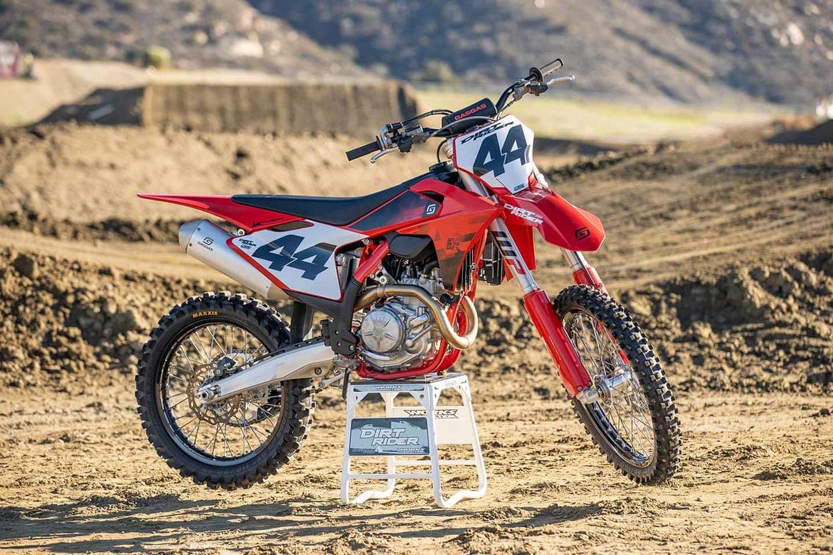 GasGas MC 450F on a dirt track stand, front three-quarter view with number 44 plates, white bodywork panels and red frame against a bermed track backdrop