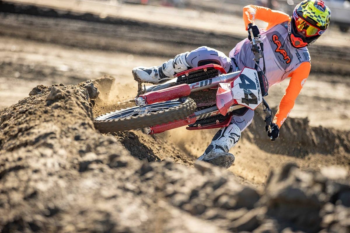 Rider in orange and white gear leaning hard into a rutted turn on a red and white GasGas MC 450F, kicking up a spray of loose dirt