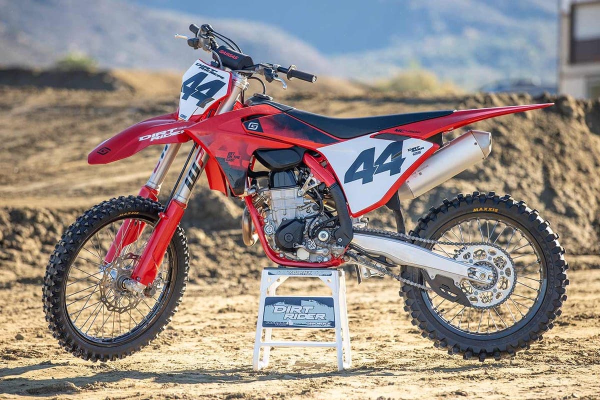 GasGas MC 450F rear three-quarter view on a track stand, showing the exhaust canister, chain and sprocket with hazy hills in the background