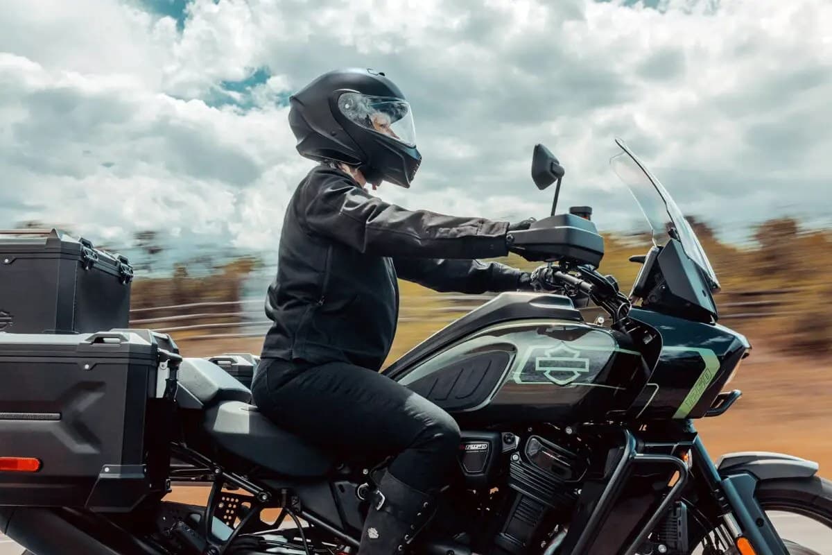 Harley-Davidson Pan America 1250 Limited in dark green, rider in black leather jacket and full-face helmet riding down an open rural road