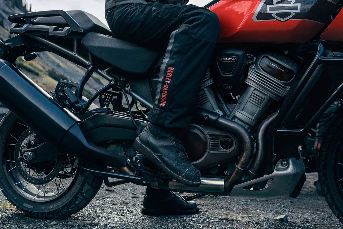 Close-up of a rider's boot on the Pan America 1250 Special's footpeg, showing the exhaust header, V-twin cylinder and rear luggage rack