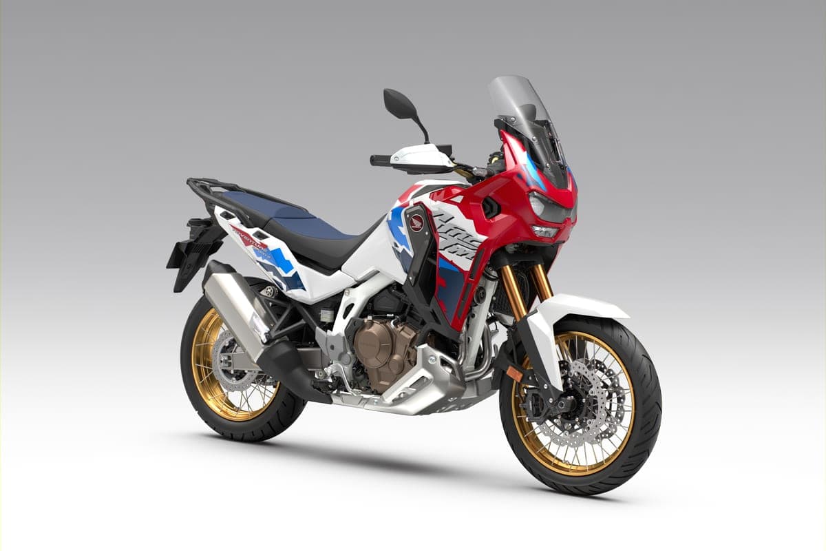 Africa Twin CRF1100L Adventure Sports in red, white and blue tricolor, front three-quarter studio view showing the tall windscreen and gold wheels