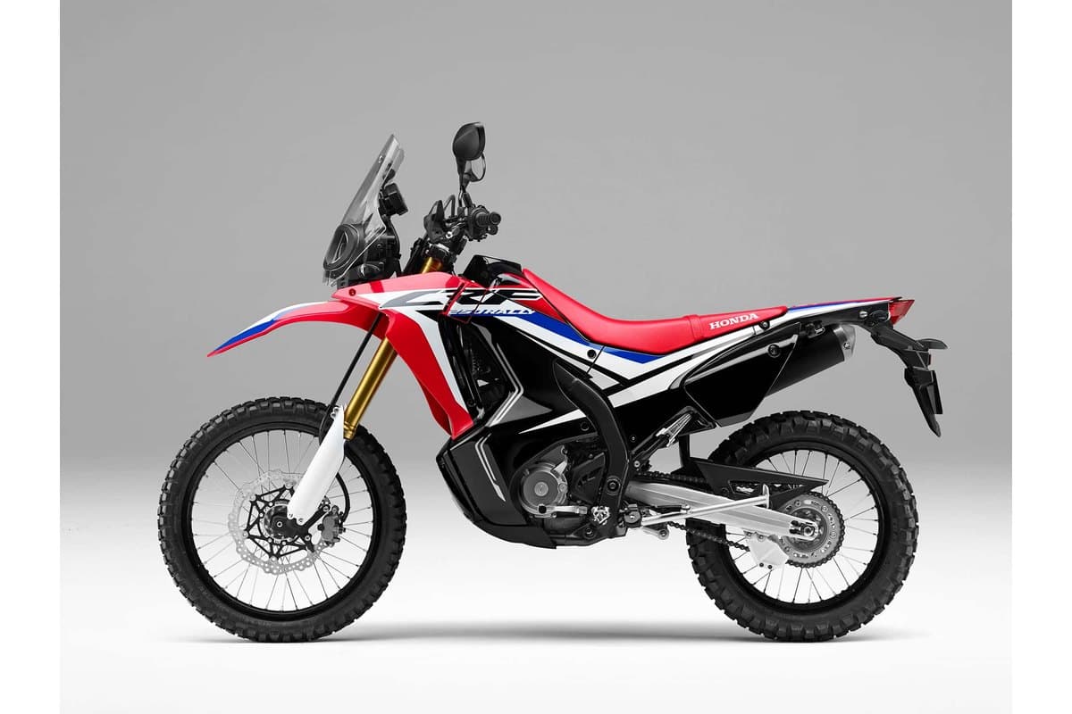 Honda CRF250L Rally in red, white and blue Rally livery, left-side studio profile against a grey background highlighting the beak fairing and exhaust