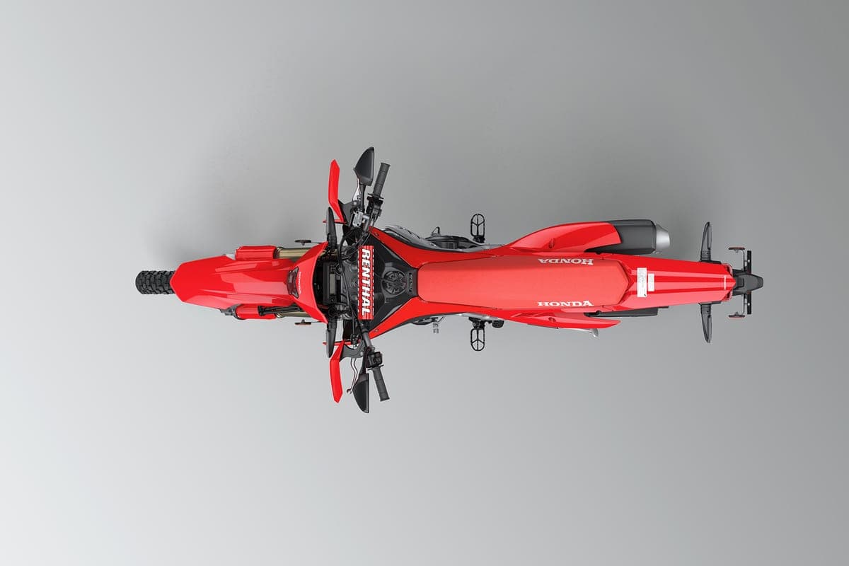 Honda CRF450RL overhead studio view showing the slim red fuel tank, silver skid area and full-length exhaust running along the frame