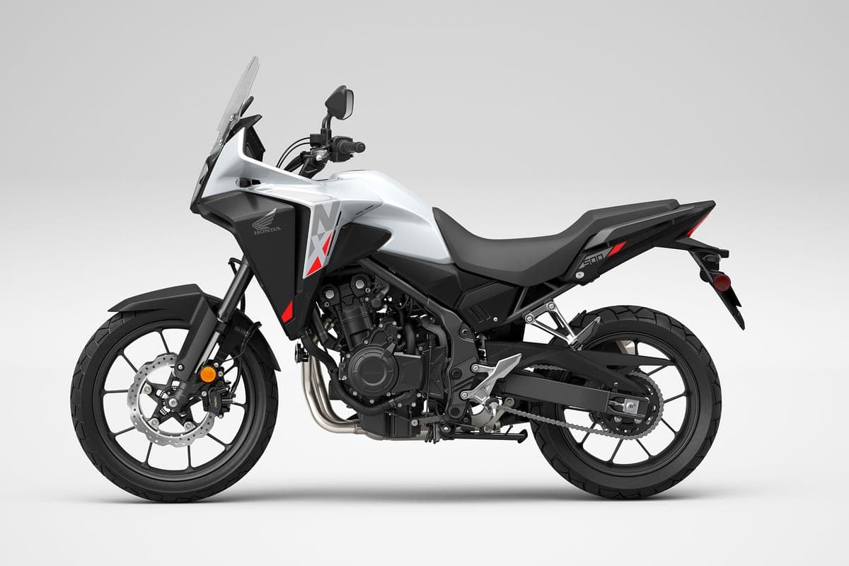 Honda NX500 in white with red accents, left-side studio profile highlighting the exposed steel exhaust headers, chain drive and beak-style front fender
