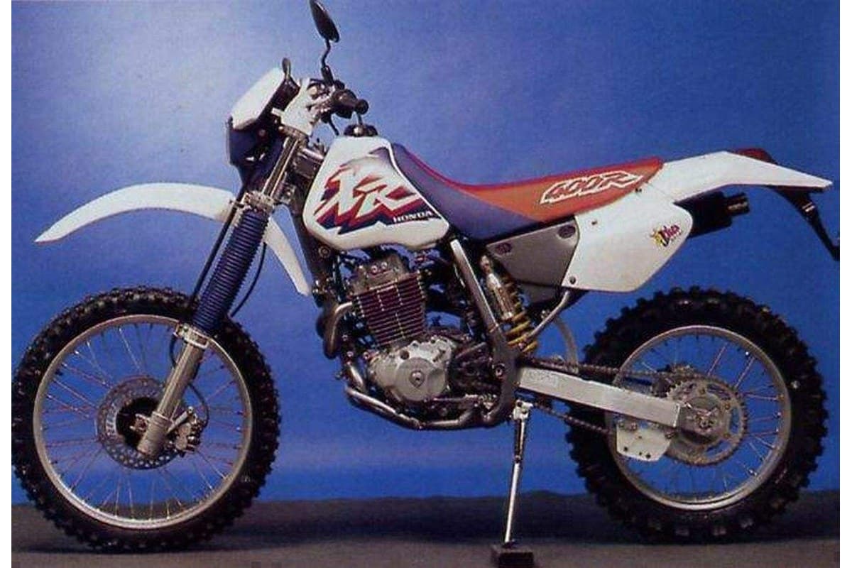 Honda XR400R in white with red seat and blue graphics, left-side view on kickstand against a blue backdrop, highlighting the rear shock and swingarm