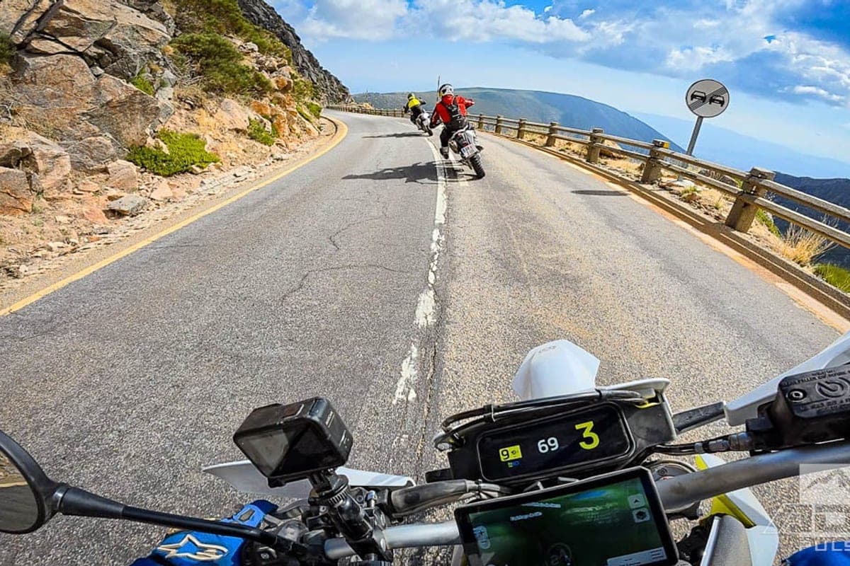 Handlebar-mounted GoPro view over the 701 Enduro's front fender along a cliffside paved switchback with two riders ahead