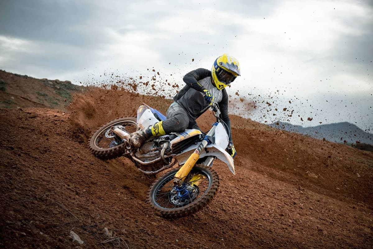 Rider cornering the Husqvarna FC 250 through a rutted red-dirt berm, roost spraying off the rear wheel
