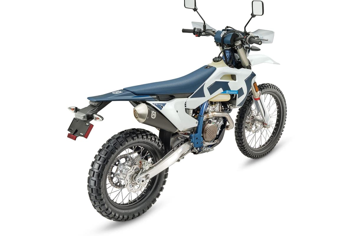 Husqvarna FE 501s rear three-quarter studio view in white and navy, showing the textured seat, rear disc brake and tucked exhaust silencer