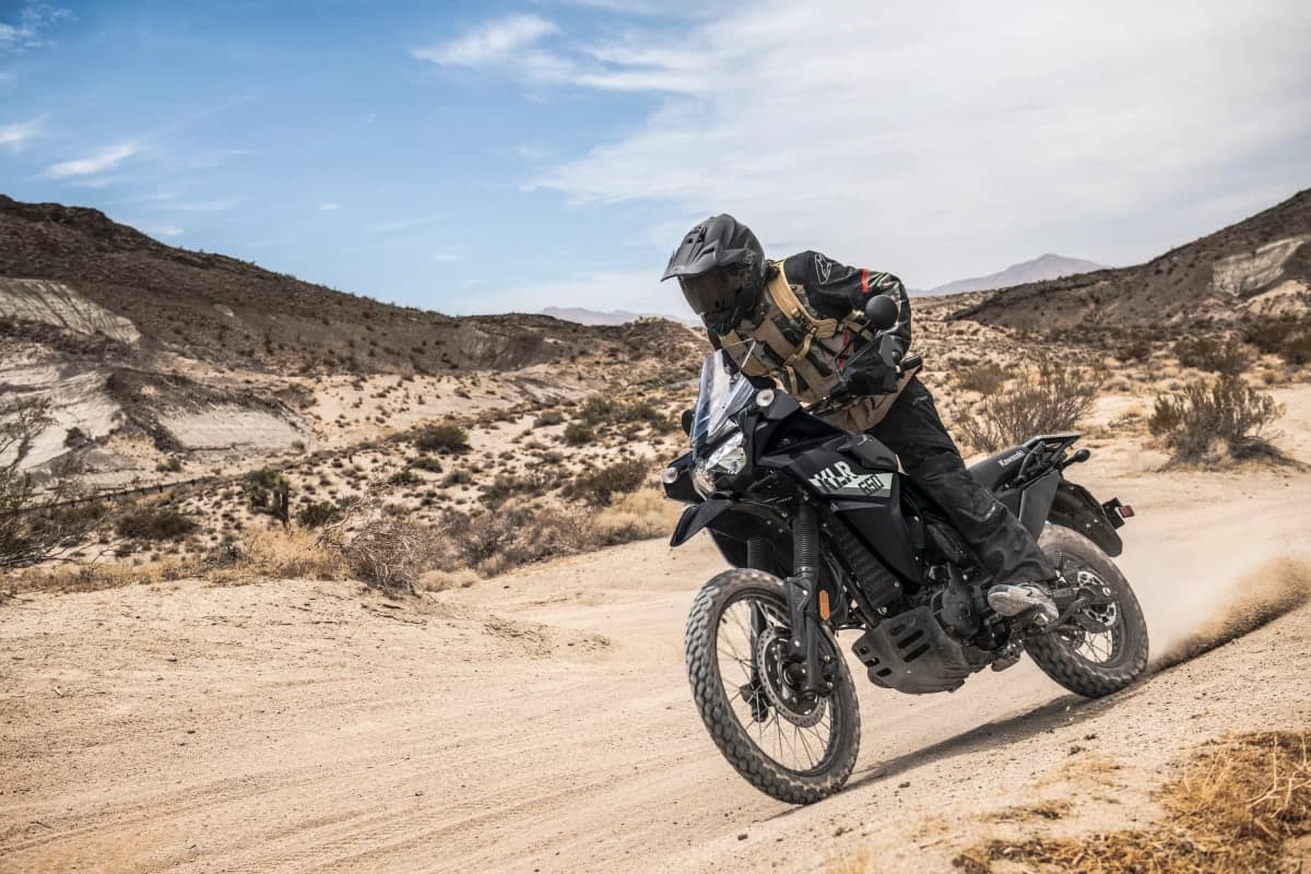 Rider kicking up dust on a black KLR650 on a desert trail