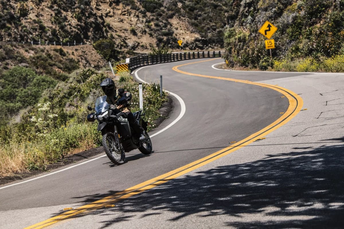 Rider on a KLR650 leaning through a curve on a winding hillside road