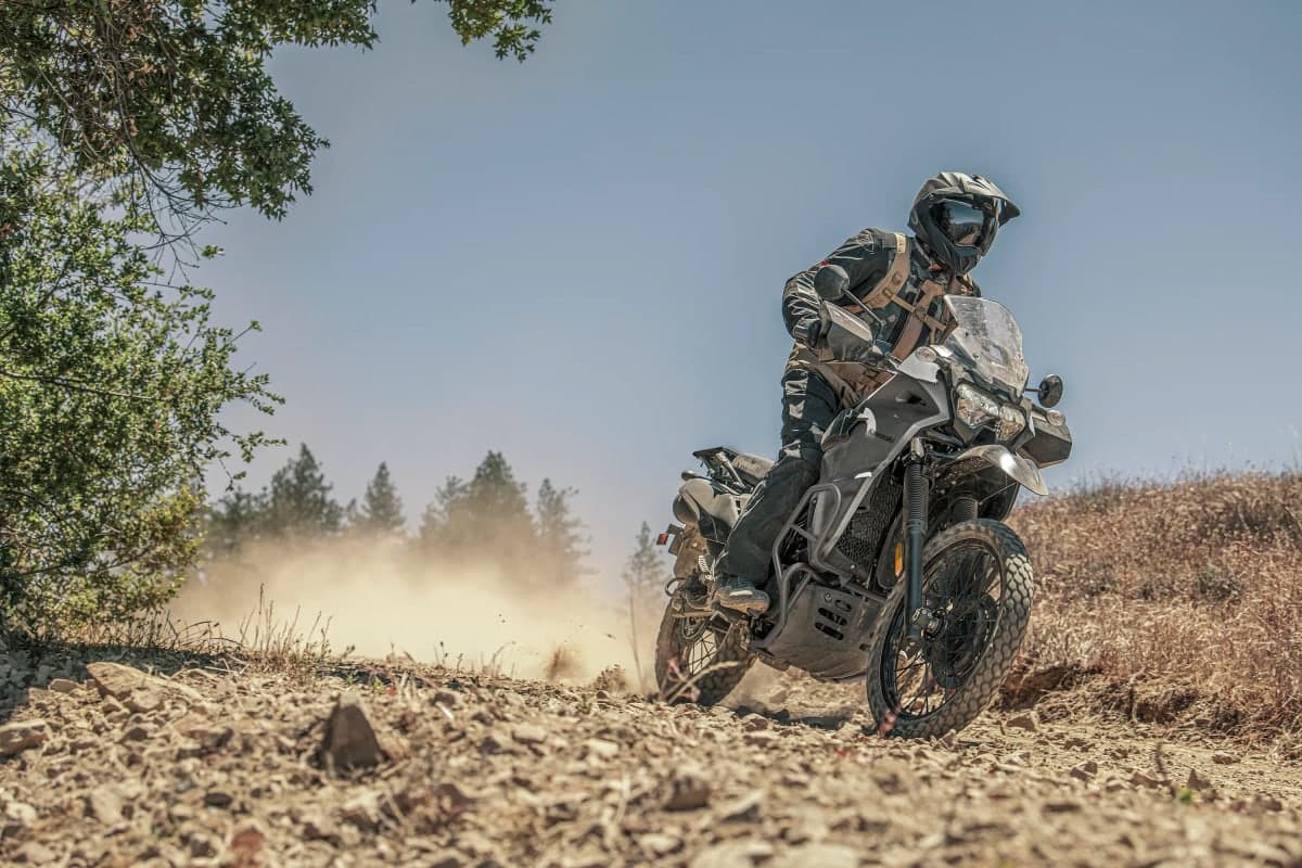 Rider kicking up dust on a KLR650 DF on a dry hillside trail
