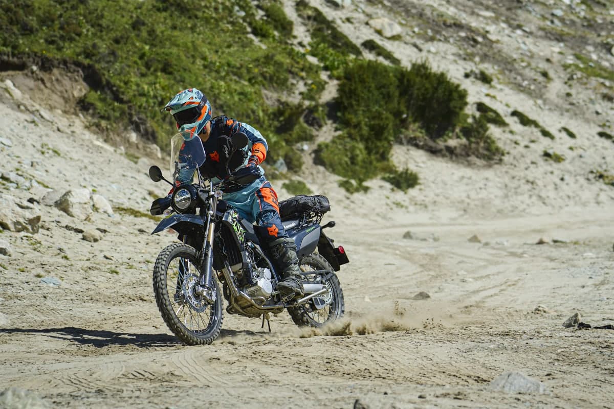 Rider with soft luggage riding a KLX300 XPL across a sandy mountain trail